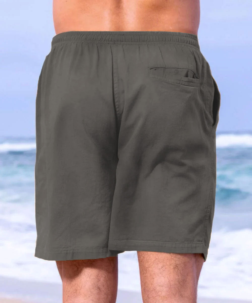 A pair of gray cotton twill shorts with an elastic waistband, deep front pockets, and a drawstring. The image features a male model wearing the shorts at a beach setting. View 3