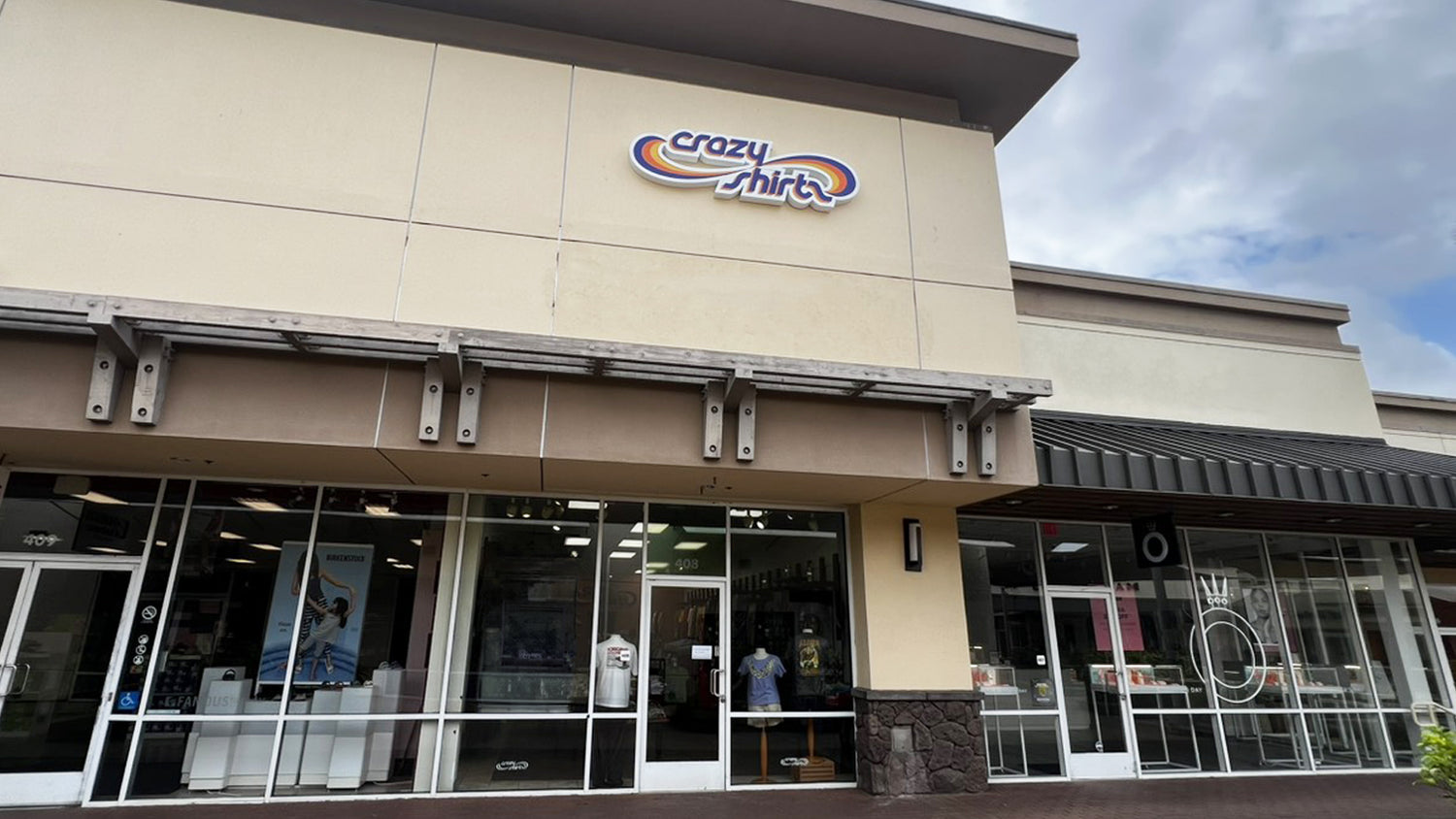 Storefront of 'crazy shirts' with large glass windows and a clear sky.