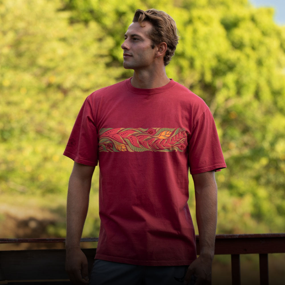 Man wearing a red t-shirt with a graphic design, standing outdoors with greenery in the background