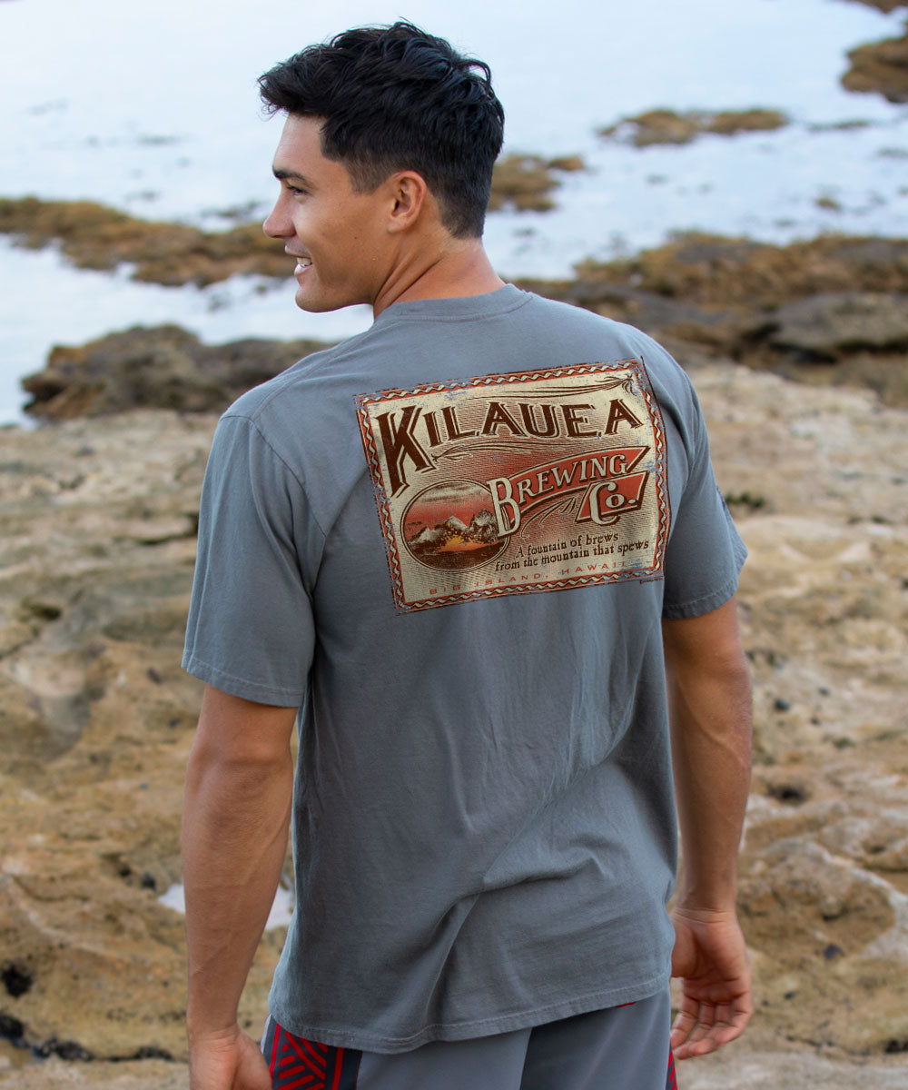 Man wearing a gray t-shirt with Kilauea Brewing Co. logo at a rocky beach. View 2