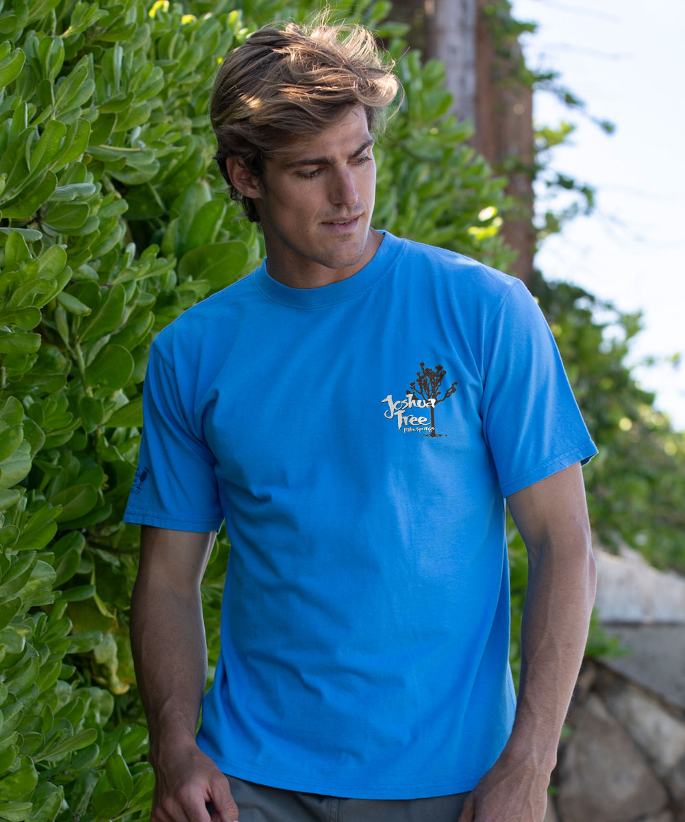 Man wearing a blue t-shirt with a logo against a green leafy background View 3