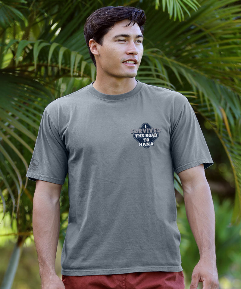 Man wearing a gray t-shirt with a logo and text, standing in front of green foliage. View 3