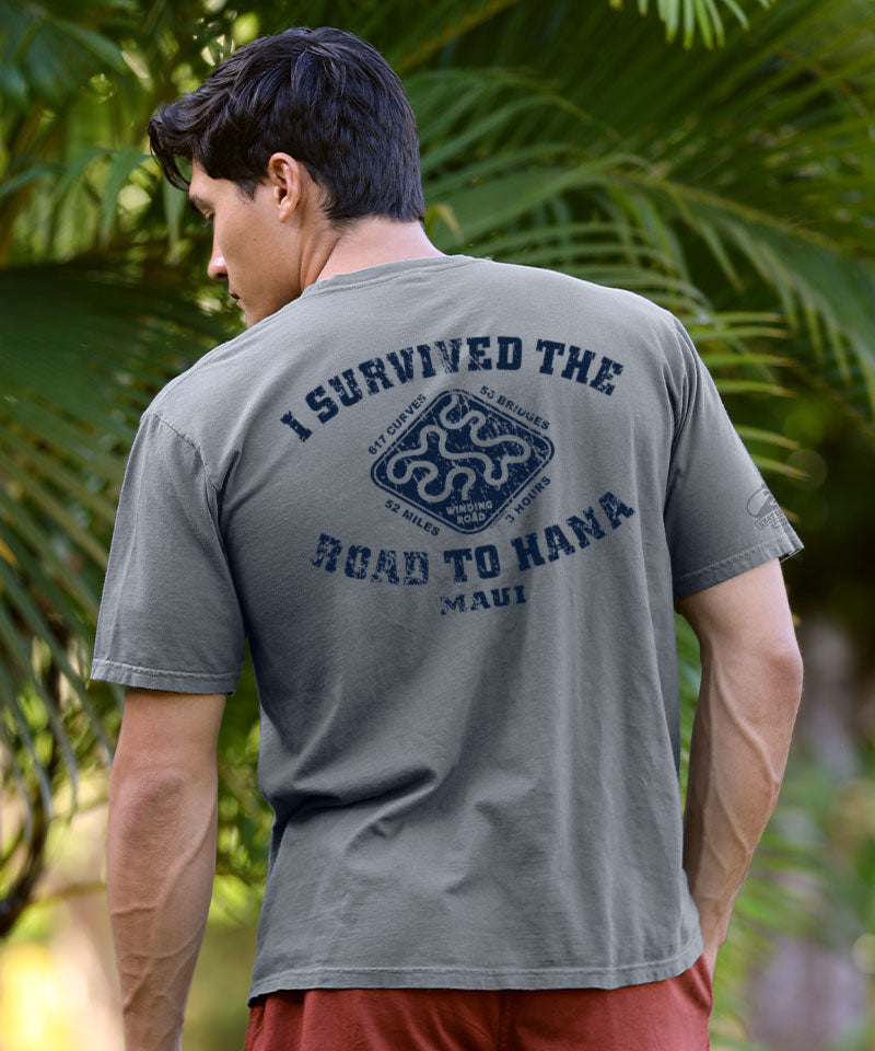 Man wearing a gray t-shirt with 'I Survived the Road to Hana Maui' text and graphic, standing outdoors with greenery. View 2