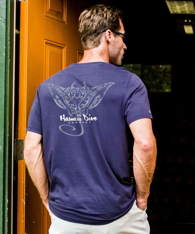 Man wearing a navy blue t-shirt with a logo and text, standing in front of a wooden door. View 2