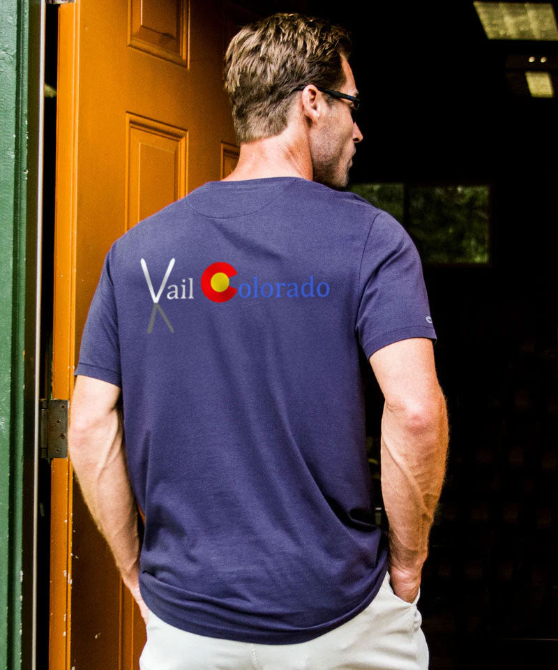 Man wearing a navy blue t-shirt with Vail Colorado logo on the back, standing in front of a wooden door. View 2