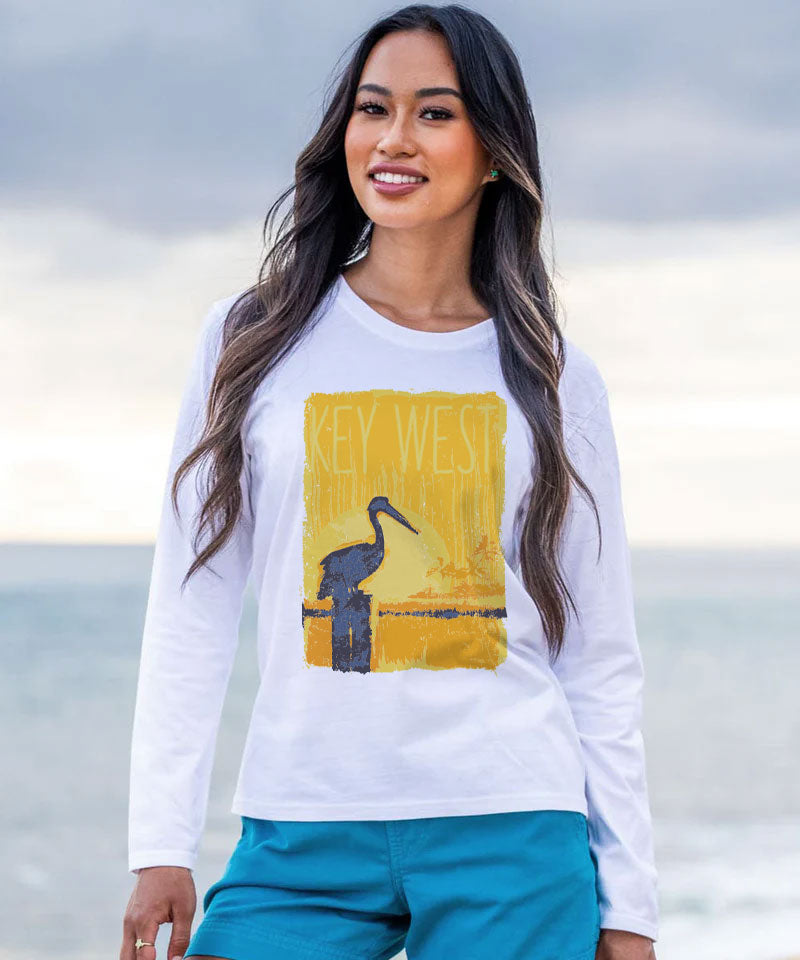 Woman wearing a white long-sleeve shirt with a Key West design on a beach. View 2