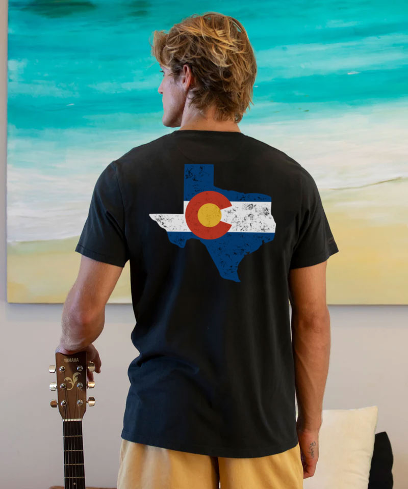 Person wearing a black t-shirt with a colorful design on the back, standing in front of a painting. View 2