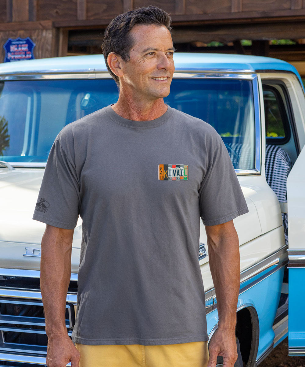 Man wearing a gray t-shirt with a logo standing next to a blue and white truck. View 3
