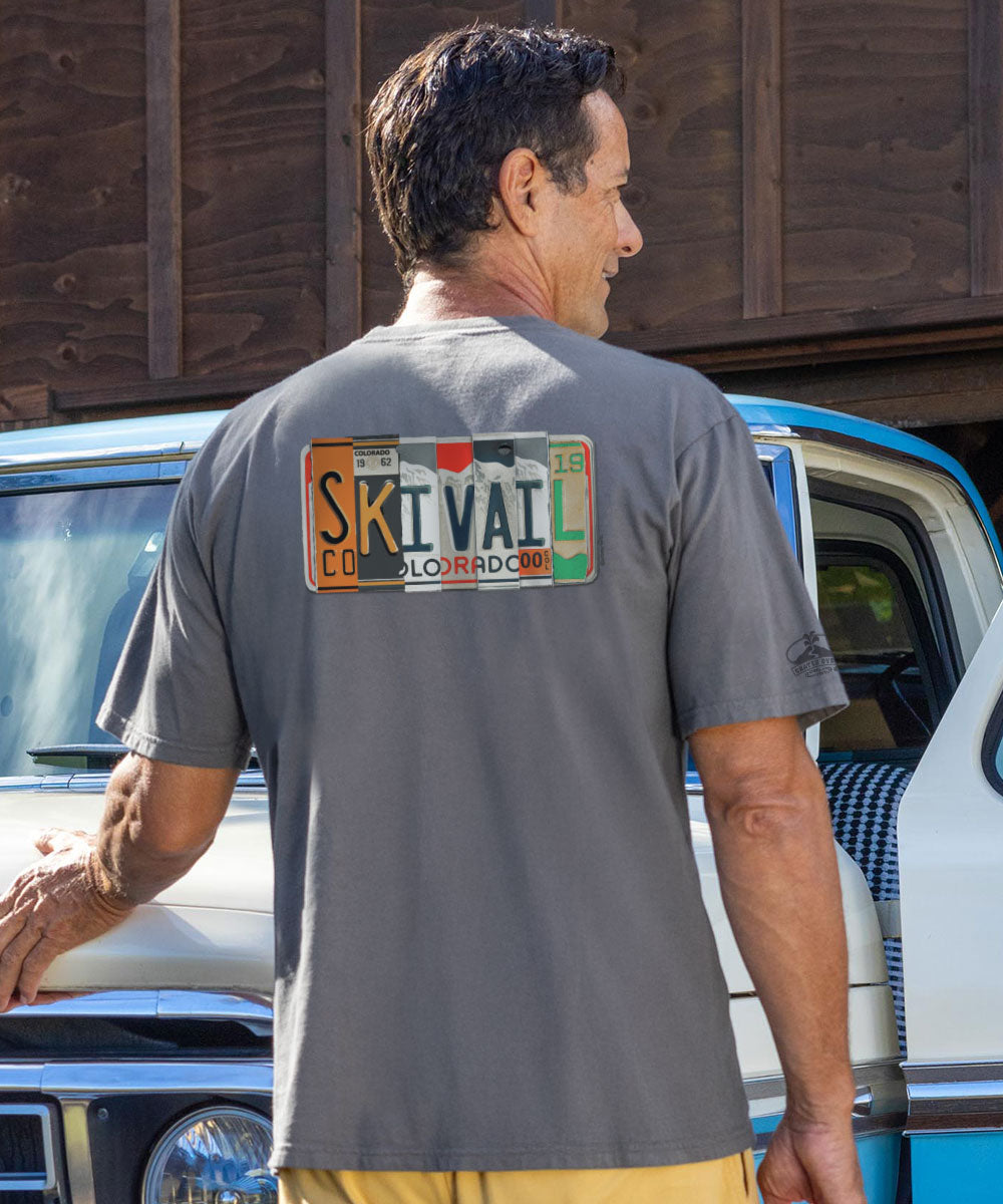 Man wearing a gray t-shirt with a license plate design, standing next to a vehicle. View 2
