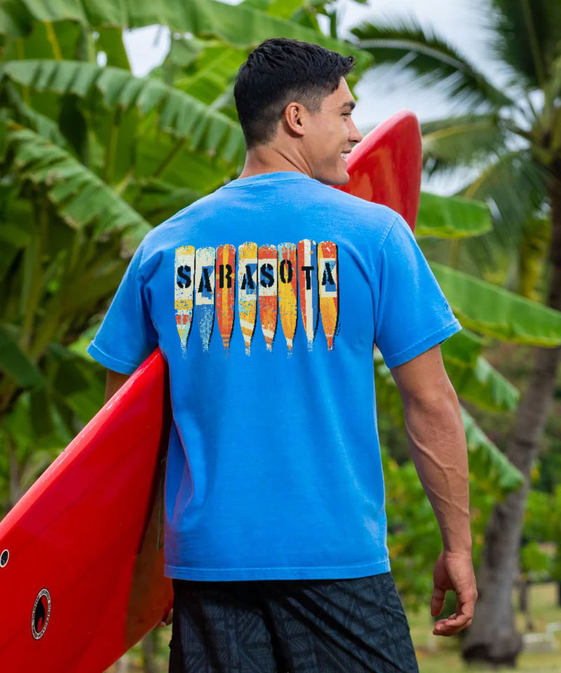 Man wearing a blue t-shirt with 'Sarasota' and colorful paddle design, holding a red kayak. View 2