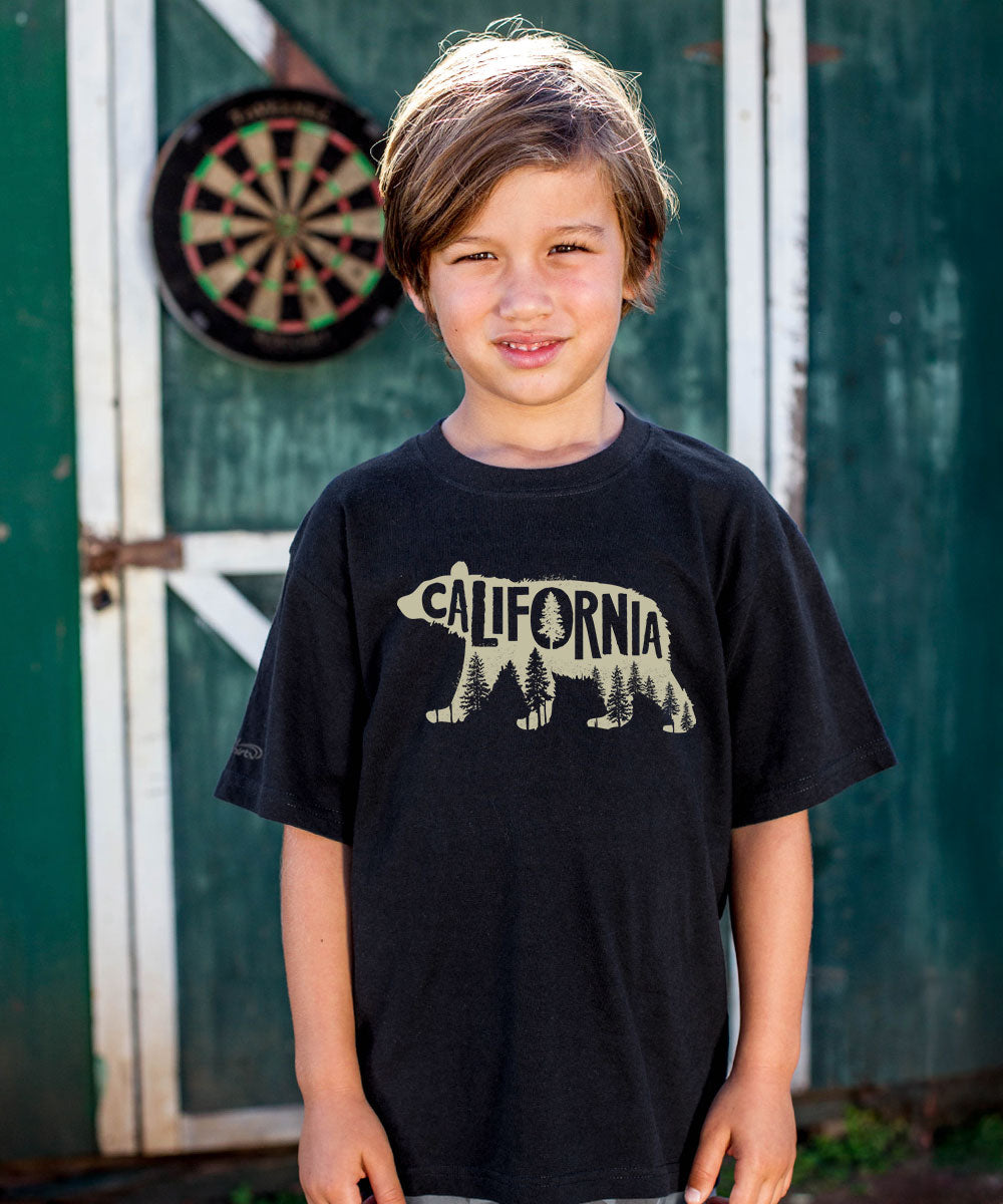 Child wearing a black t-shirt with a bear and 'California' graphic, standing in front of a green door. View 2