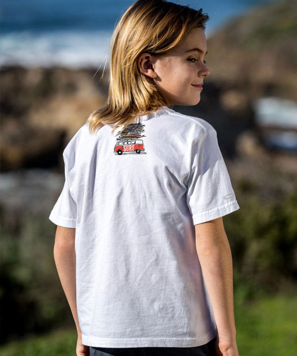 A child wearing a white short-sleeve t-shirt with a small graphic print on the back, photographed outdoors against a blurred coastal background. View 3