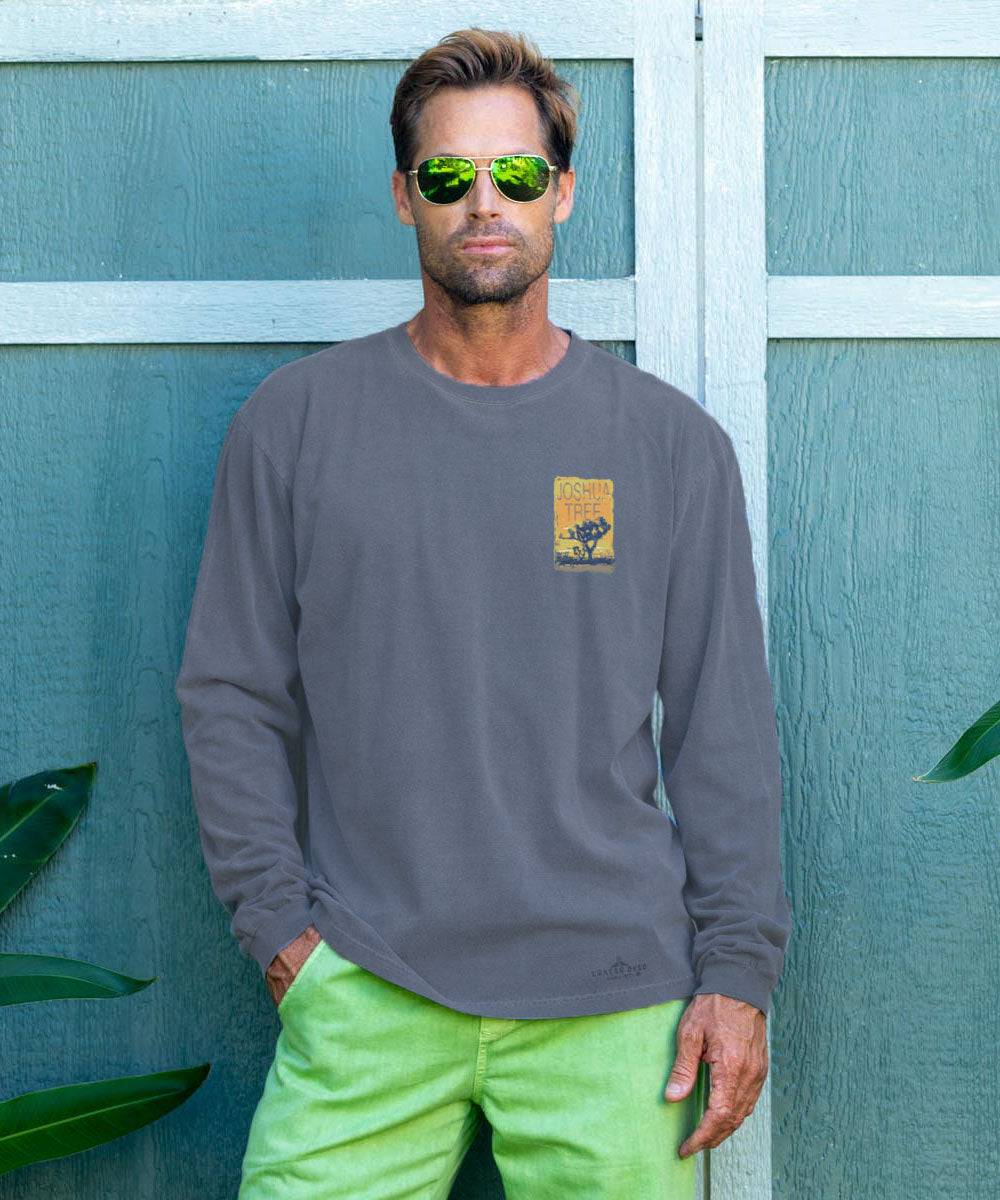 Man wearing a gray long-sleeve shirt with a logo and green pants standing against a teal wall. View 3