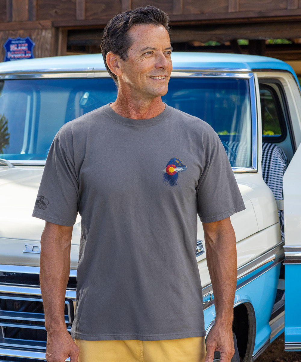 Man wearing a gray t-shirt with a logo standing next to a blue and white van. View 3