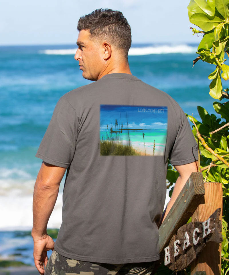 Man wearing a gray t-shirt with a beach scene print, standing by the ocean. View 2