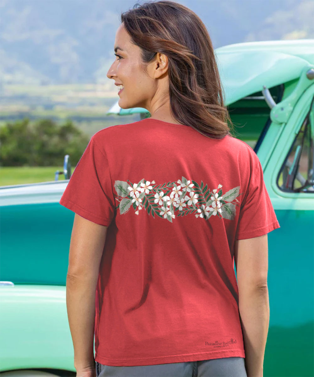 Woman wearing a red t-shirt with floral design in front of a vintage green truck. View 3