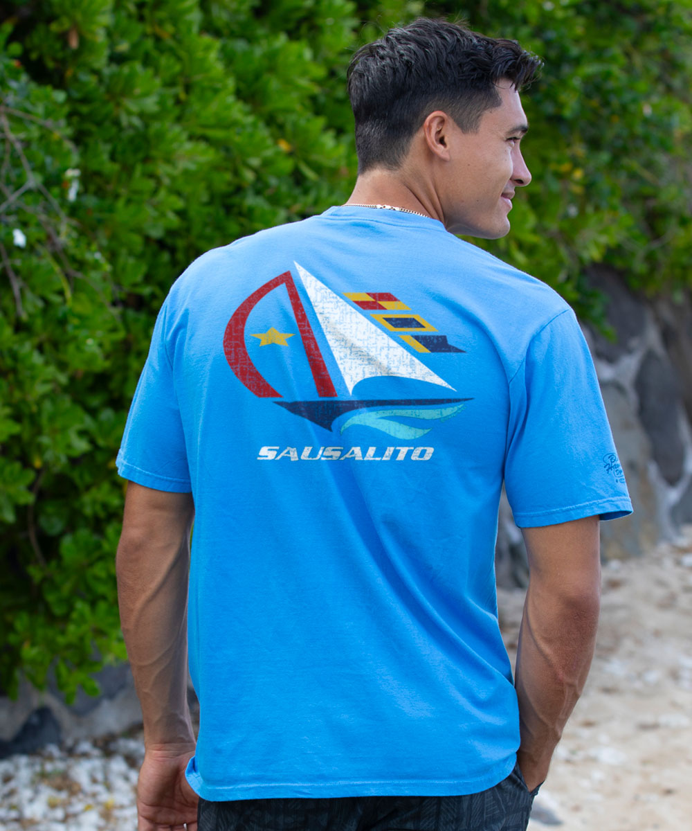 Man wearing a blue t-shirt with a sailboat design and 'Sausalito' text on the back, standing outdoors. View 2