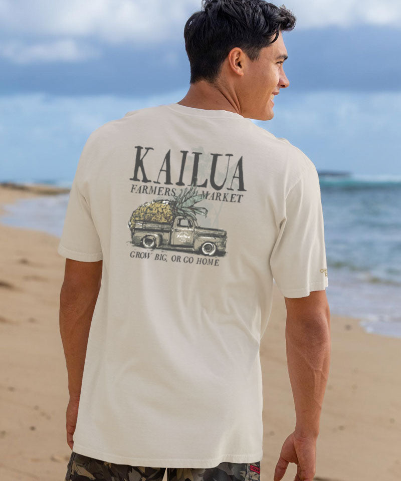 Man wearing a white t-shirt with 'Kailua Farmers Market' graphic on a beach View 2