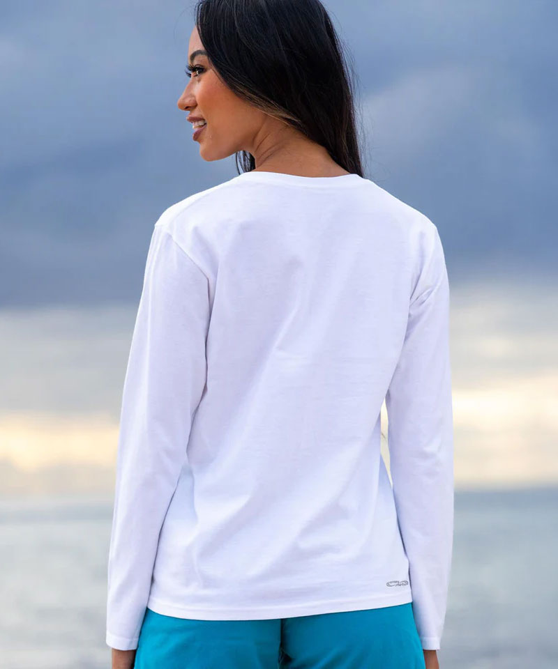 Woman wearing a white long-sleeve shirt and teal pants against a blurred natural background View 3