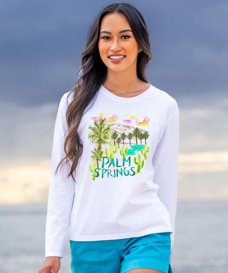 Woman wearing a white long-sleeve shirt with 'Palm Springs' design on a beach. View 2