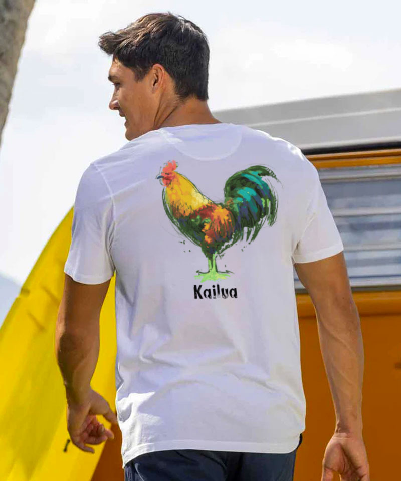 Man wearing a white t-shirt with a colorful rooster design and 'Kailua' text, with a yellow surfboard in the background View 2
