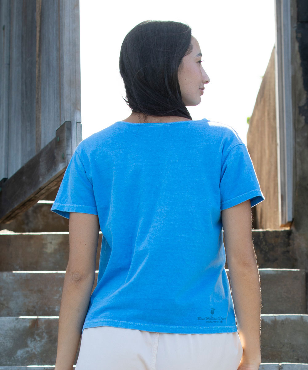 Person wearing a blue t-shirt with a logo on the back, standing on steps. View 3