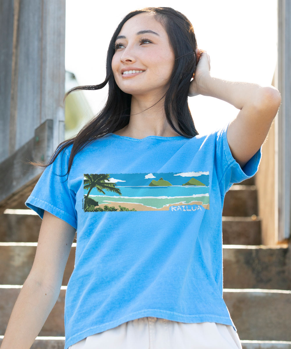 Woman wearing a blue t-shirt with a scenic design and 'Kailua' text, standing outdoors. View 2