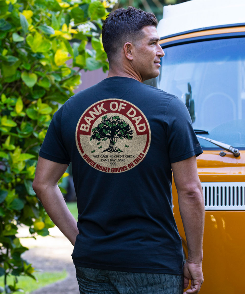 Man wearing a black t-shirt with 'Bank of Dad' graphic, standing next to a vintage van.