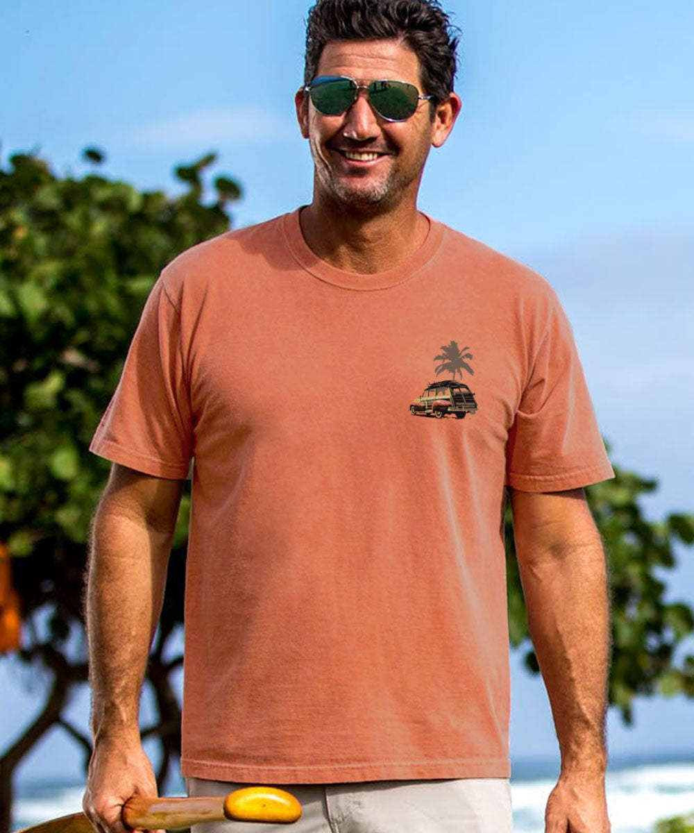 Man wearing a light red t-shirt with a palm tree design, standing outdoors with trees and blue sky in the background. View 3