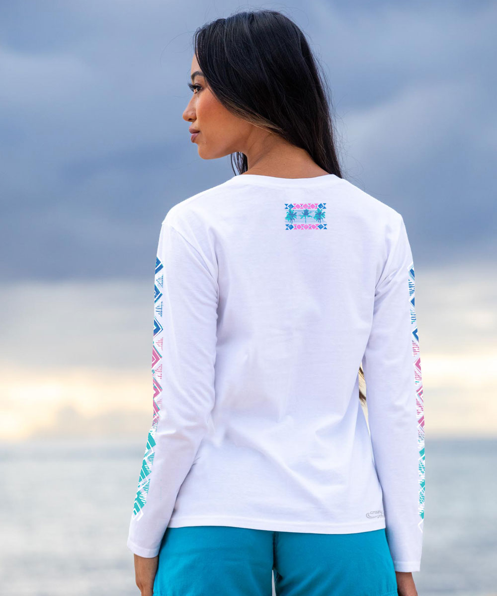 Woman wearing a white long-sleeve shirt with colorful designs on the sleeves and back, standing against a cloudy sky. View 3