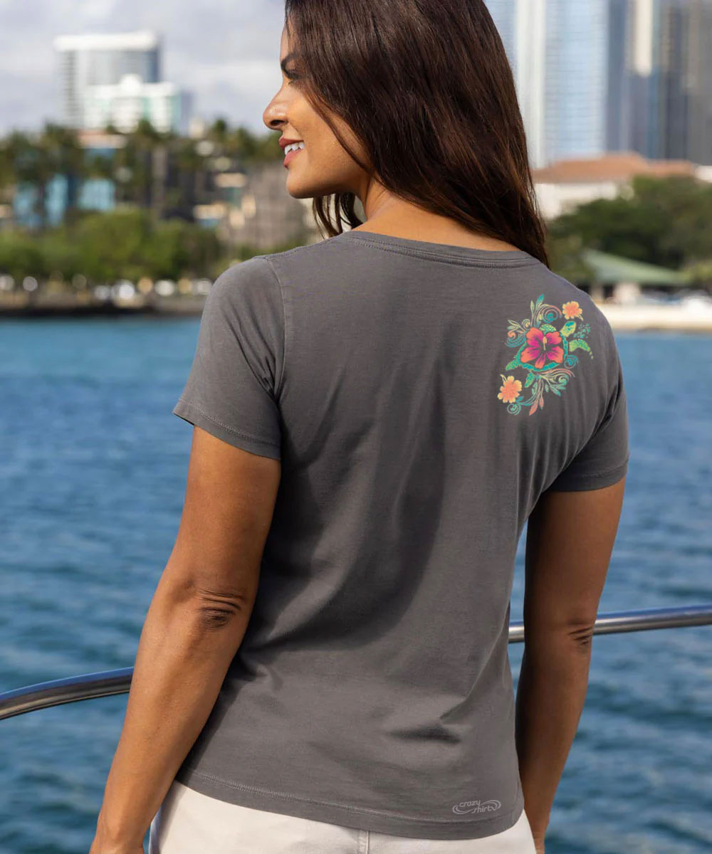 Woman wearing a gray t-shirt with a floral design on the shoulder, looking out at the sea View 3