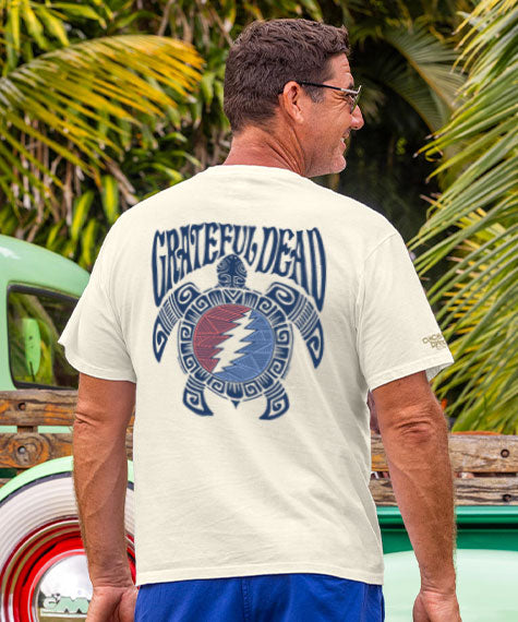 Man wearing a 'Grateful Dead' t-shirt with a turtle design, standing in front of a vintage truck and palm trees. View 2