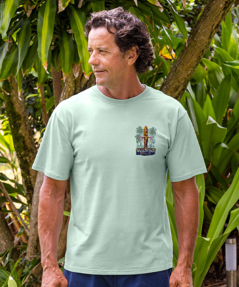 Man wearing a light green t-shirt with a logo in a tropical setting View 3