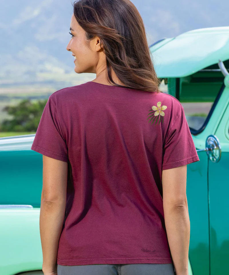Woman wearing a maroon t-shirt with a flower design in front of a vintage green car. View 3