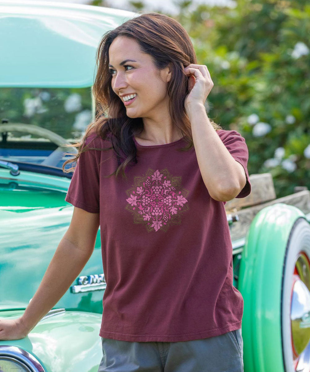 Woman wearing a maroon t-shirt with a pink floral design, standing next to a vintage car. View 2