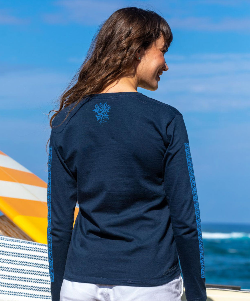 Woman wearing a navy blue long-sleeve shirt with a logo on the back, standing by the ocean. View 3