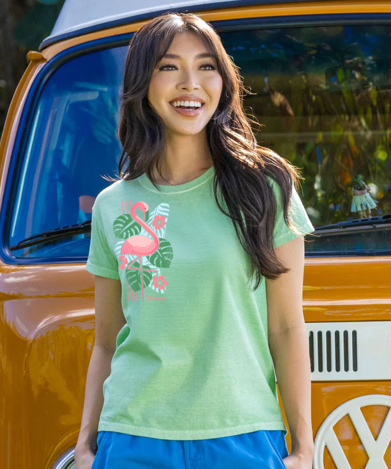 Woman wearing a green t-shirt with a flamingo design in front of a vintage van. View 2