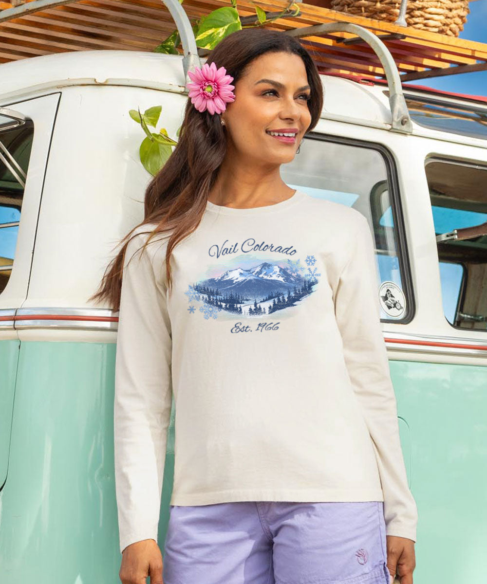 Woman wearing a long-sleeve shirt with a mountain graphic and text, standing in front of a vintage van. View 2