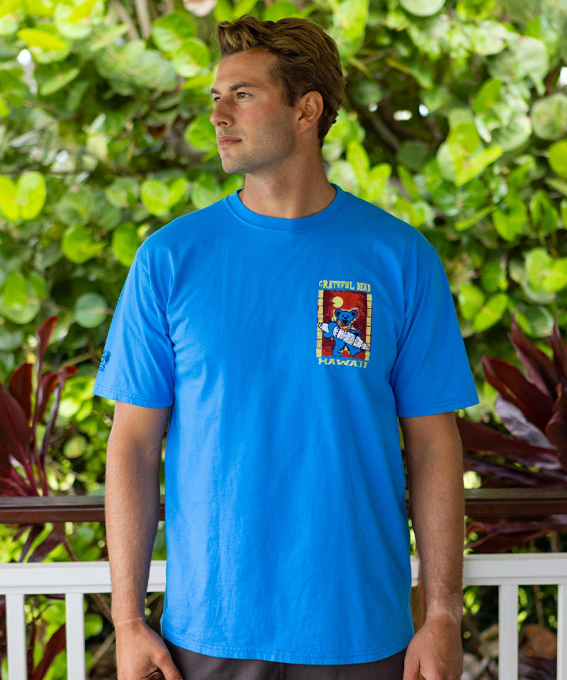 Man wearing a blue t-shirt with a graphic design in front of green foliage View 3
