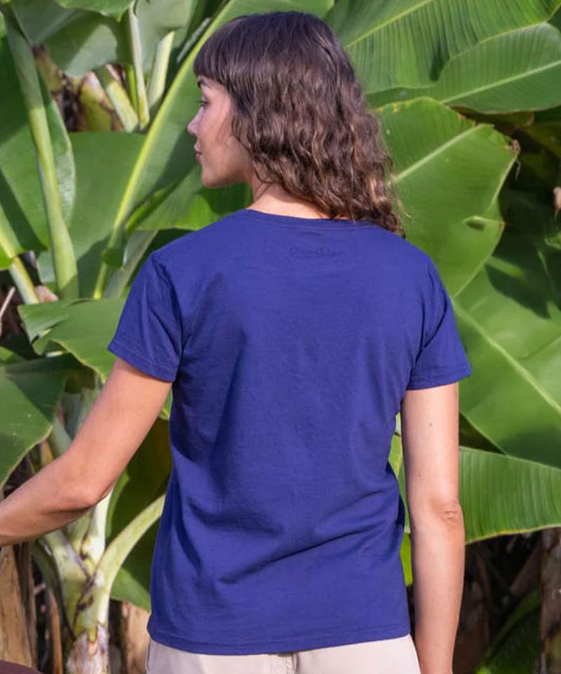 woman wearing a purple t-shirt in front of green foliage. View 3