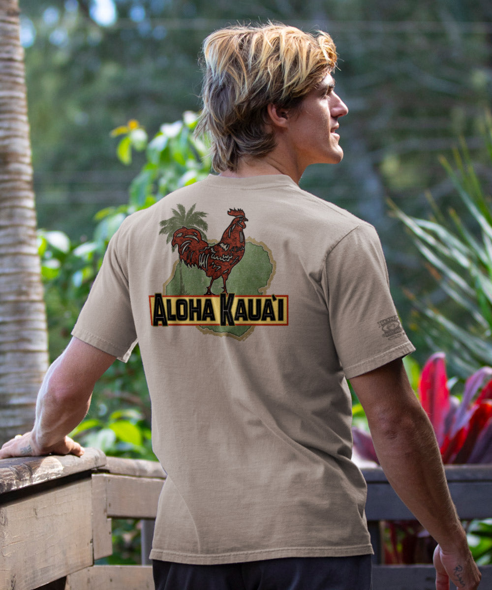 Man wearing beige t-shirt with a rooster design on the back standing in front of foliage