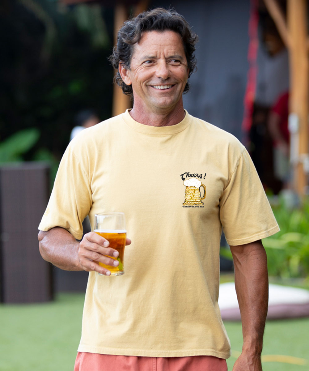 Man holding a beer and wearing a light yellow t-shirt with a graphic design outdoors. View 3