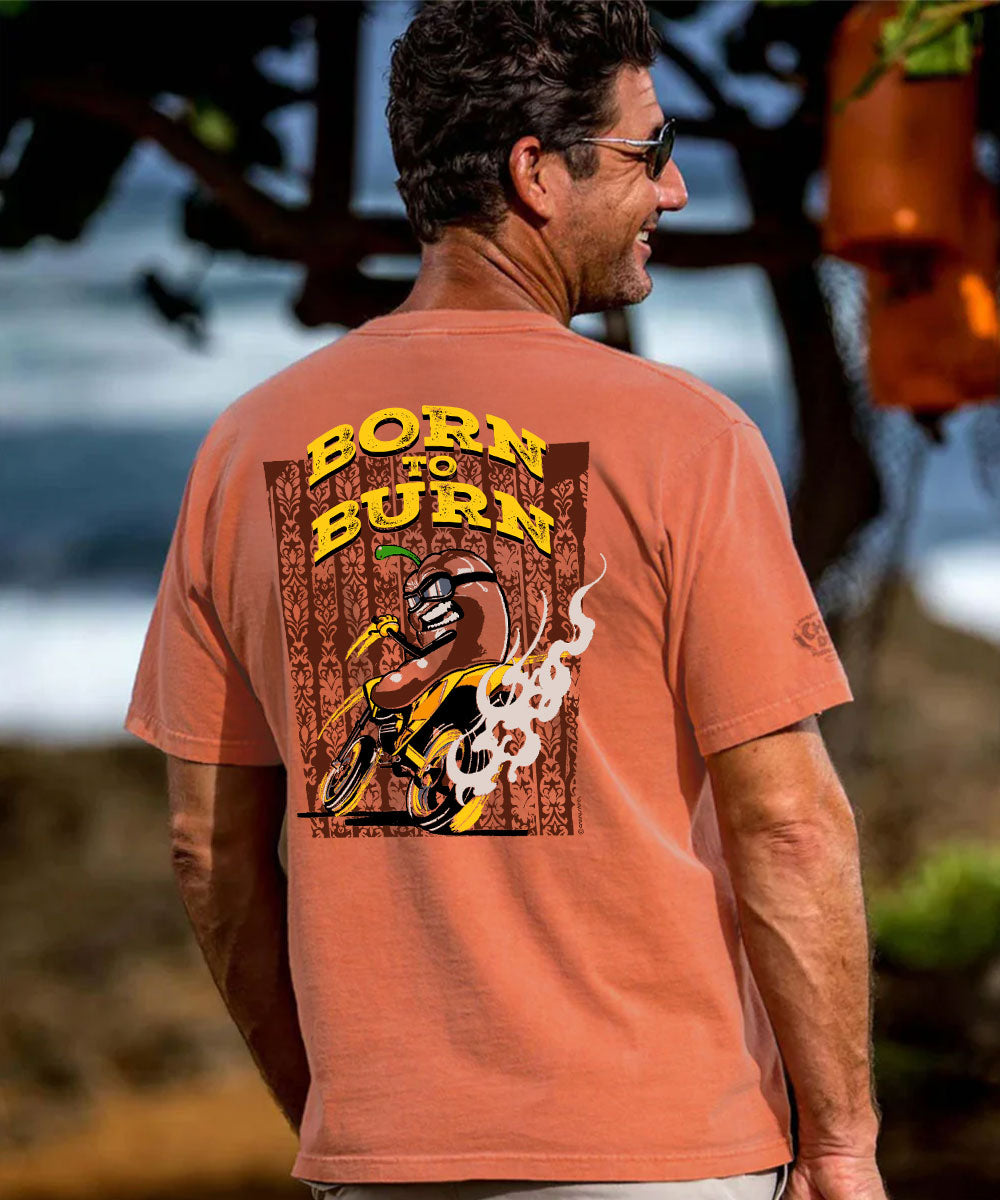 A man wearing a terracotta orange t-shirt, viewed from behind to show the back graphic. The graphic features the text 'BORN TO BURN' in yellow over a brown wood-textured background with a cartoon motorcycle and flame illustration. View 2