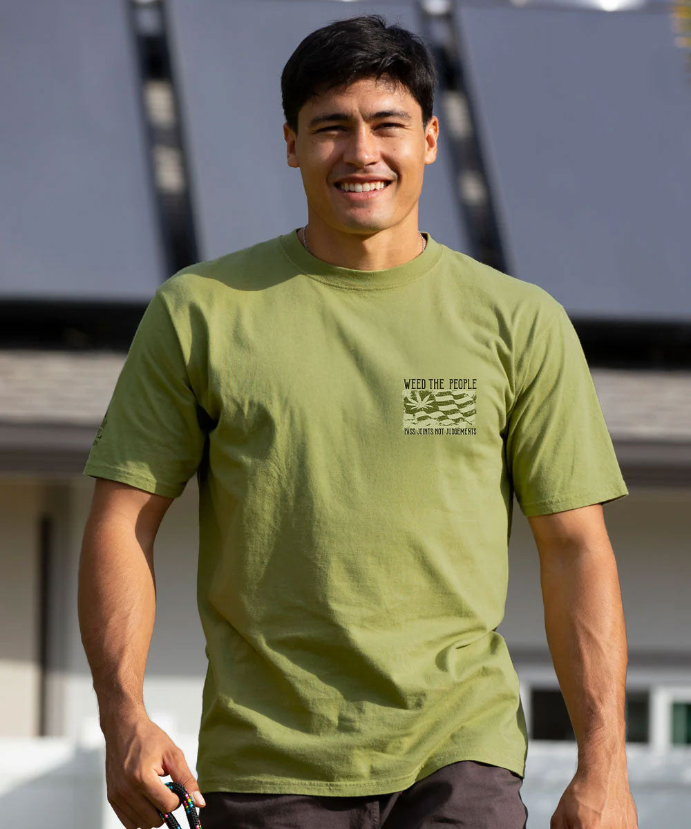 A smiling man wearing an olive green crewneck t-shirt with a small chest graphic that reads 'WITH THE PEOPLE WE HAVE THE CHANCE' and 'HAWAIIAN MADE'. View 3