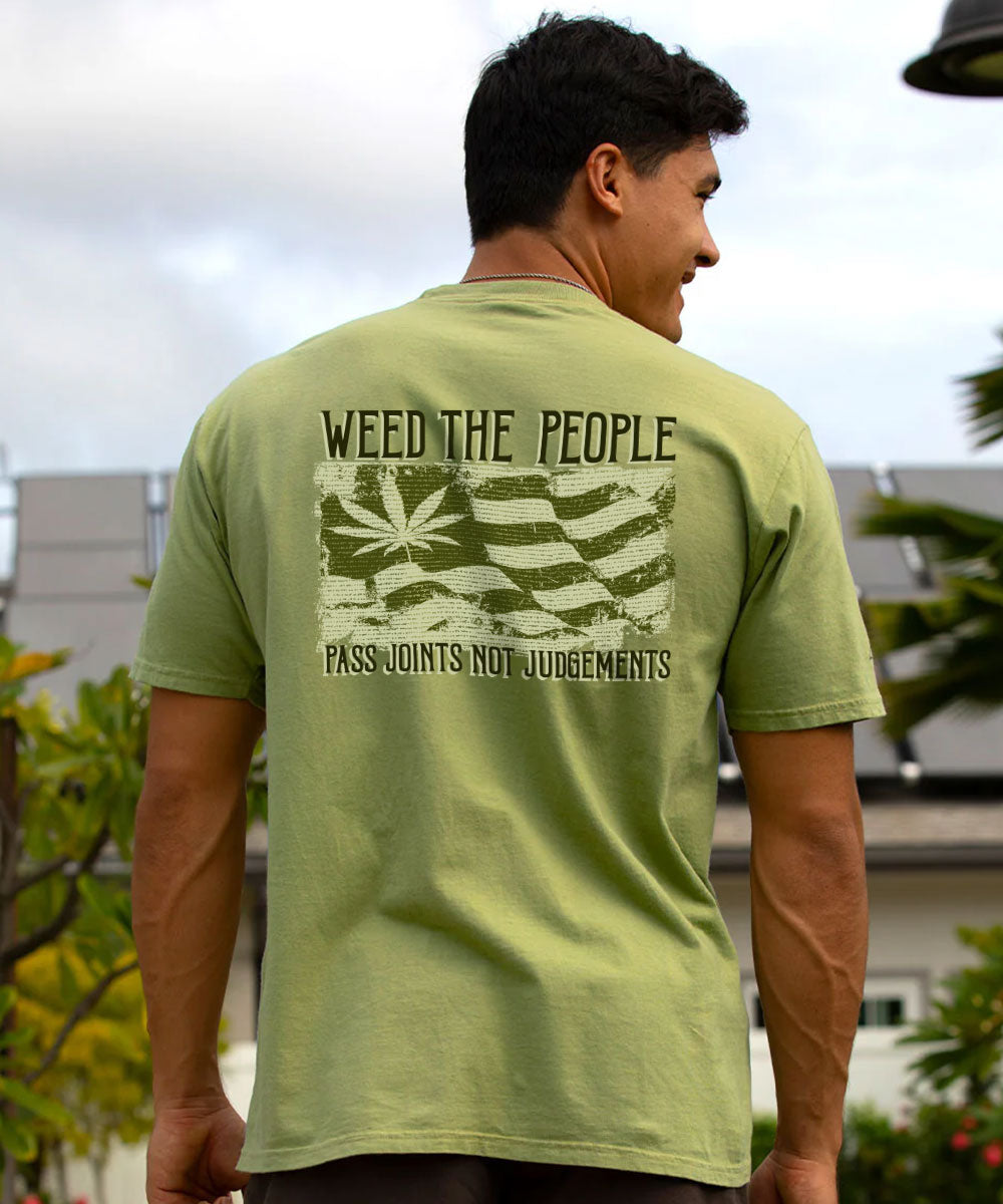 A man viewed from behind wearing a light olive green t-shirt with a distressed graphic on the back. The graphic features a stylized American flag with a marijuana leaf in the canton and the text 'WEED THE PEOPLE' and 'PASS JOINTS NOT JUDGEMENTS'. View 2