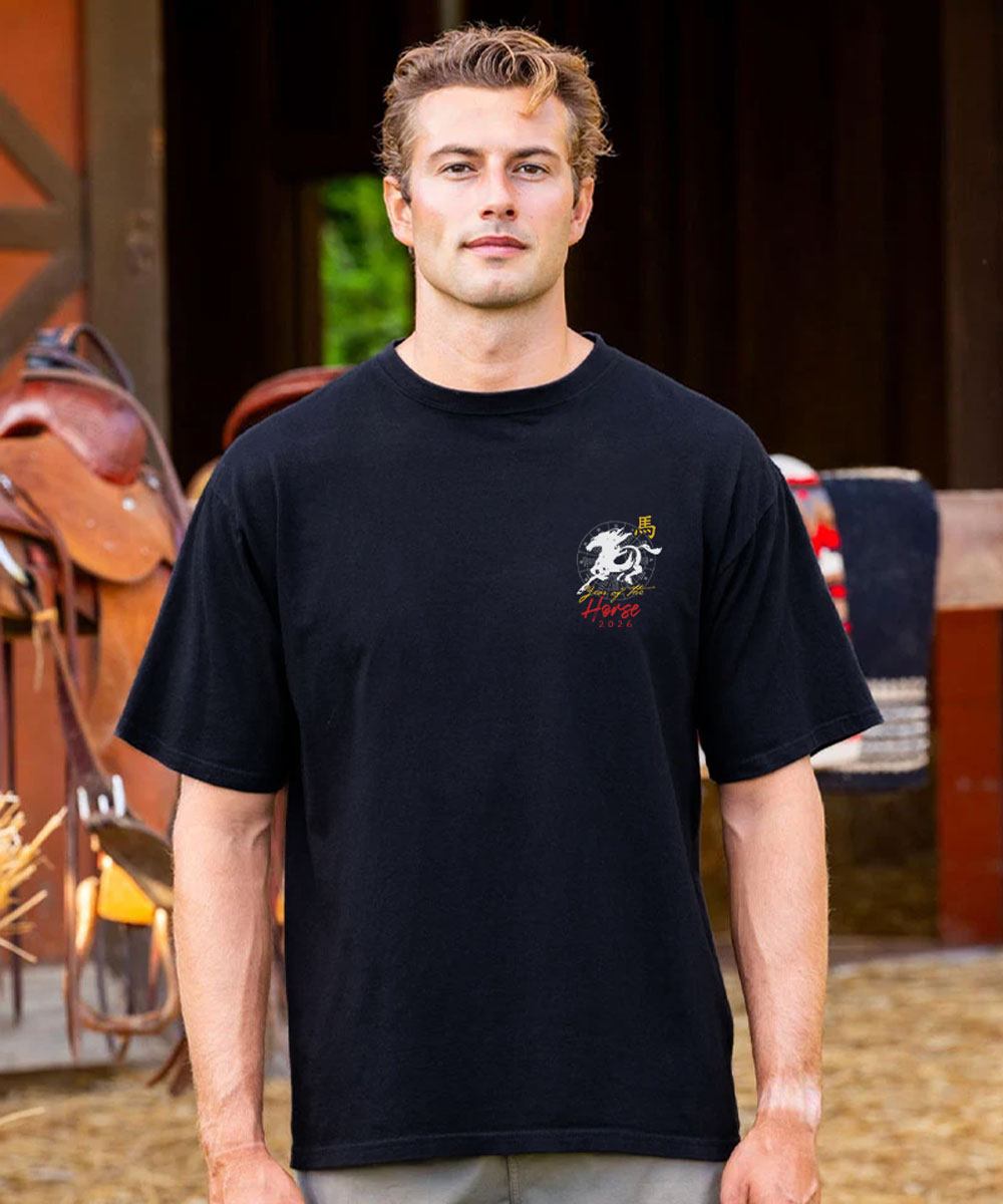Man wearing a black t-shirt with a logo in front of a barn View 3