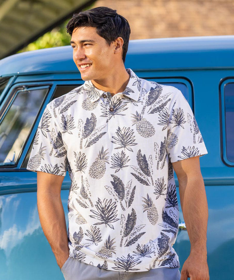 Man wearing a pineapple pattern white polo shirt standing next to a blue vehicle