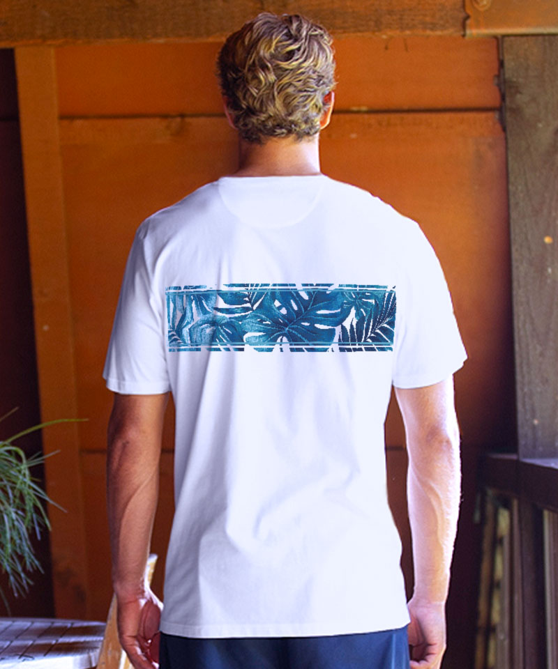 Person wearing a white t-shirt with a blue tropical design on the back, standing in front of a wooden door. View 3