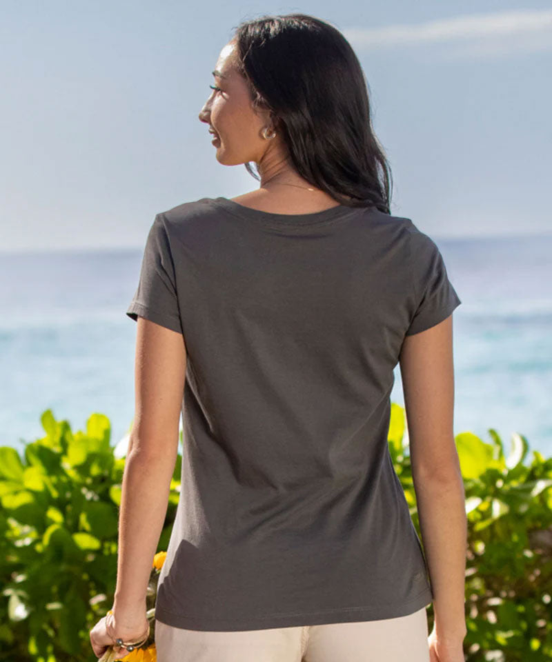 Woman wearing a gray t-shirt standing by the ocean with greenery around View 3