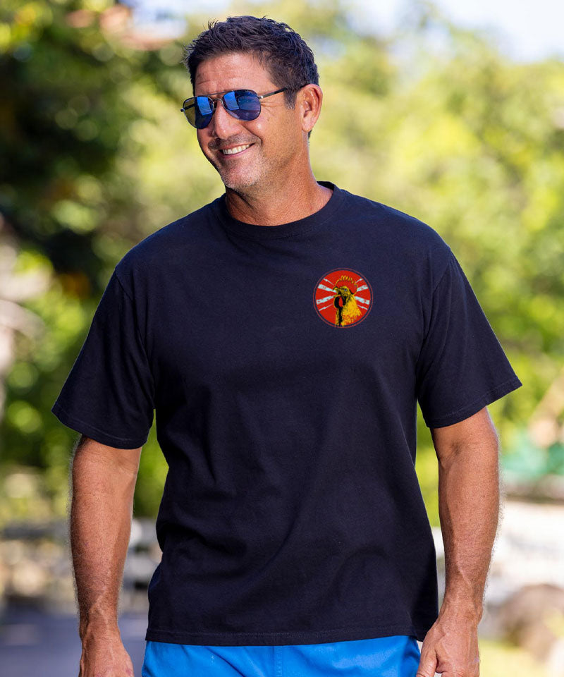 Man wearing a black t-shirt with a small logo on the front, standing outside. View 3